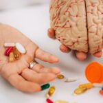 Person holding pills in one hand and a brain model in the other.