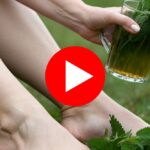 Woman holding a glass of herbal drink with fresh leaves.