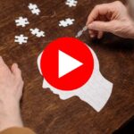 Elderly person arranging puzzle pieces on a brain-shaped board.