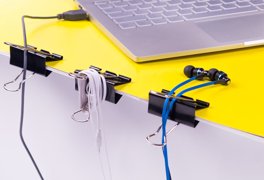 binder clips attached to the edge of a desk, used to organize cables and earphones neatly near a laptop.