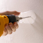 a person is holding a yellow drill with a plastic cup attached to catch dust while drilling into a wall.