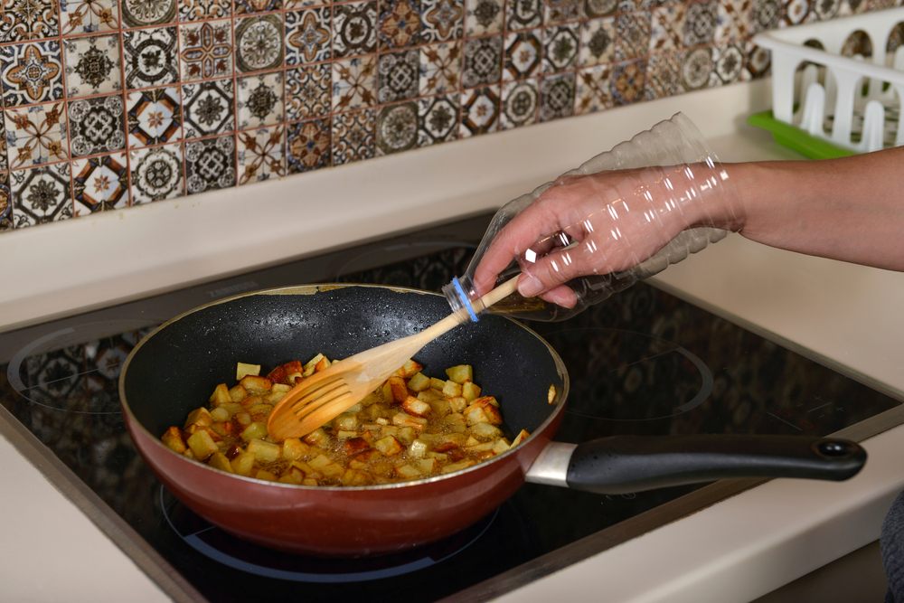 a person using a cut plastic bottle as a DIY splatter guard while stirring food in a frying pan on a stovetop.