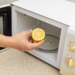 a person is placing half a lemon into a microwave to use it for the cleaning purposes.