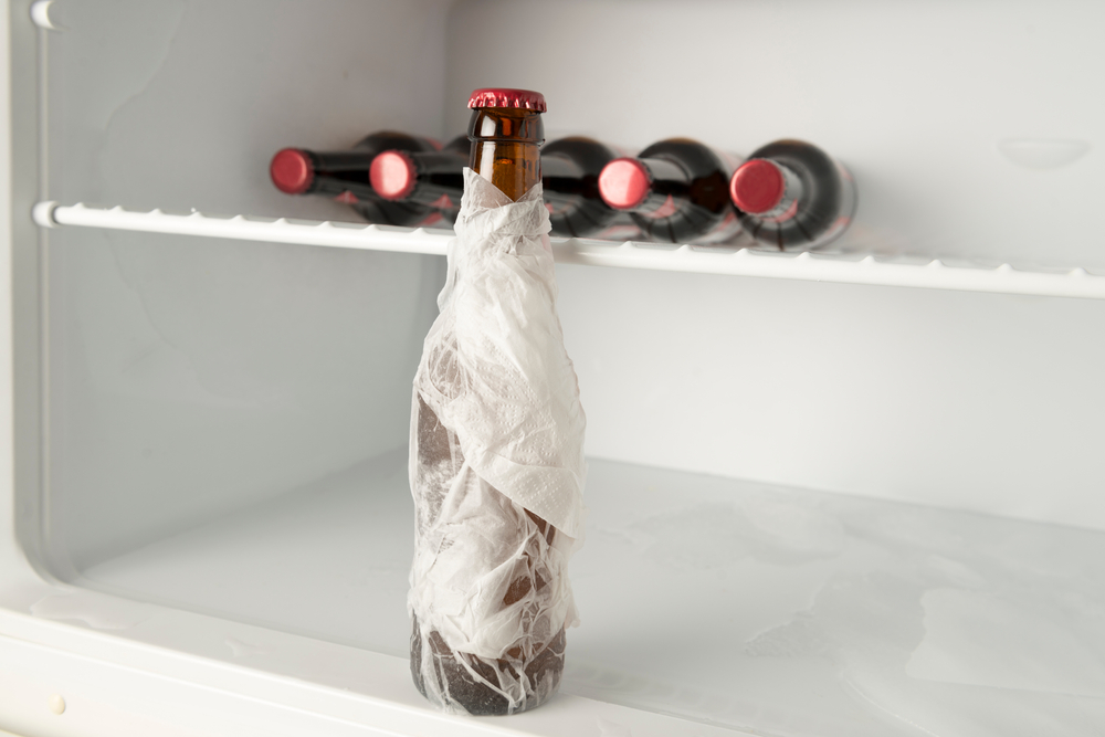 a beer bottle wrapped in a damp paper towel placed inside a refrigerator for rapid cooling.