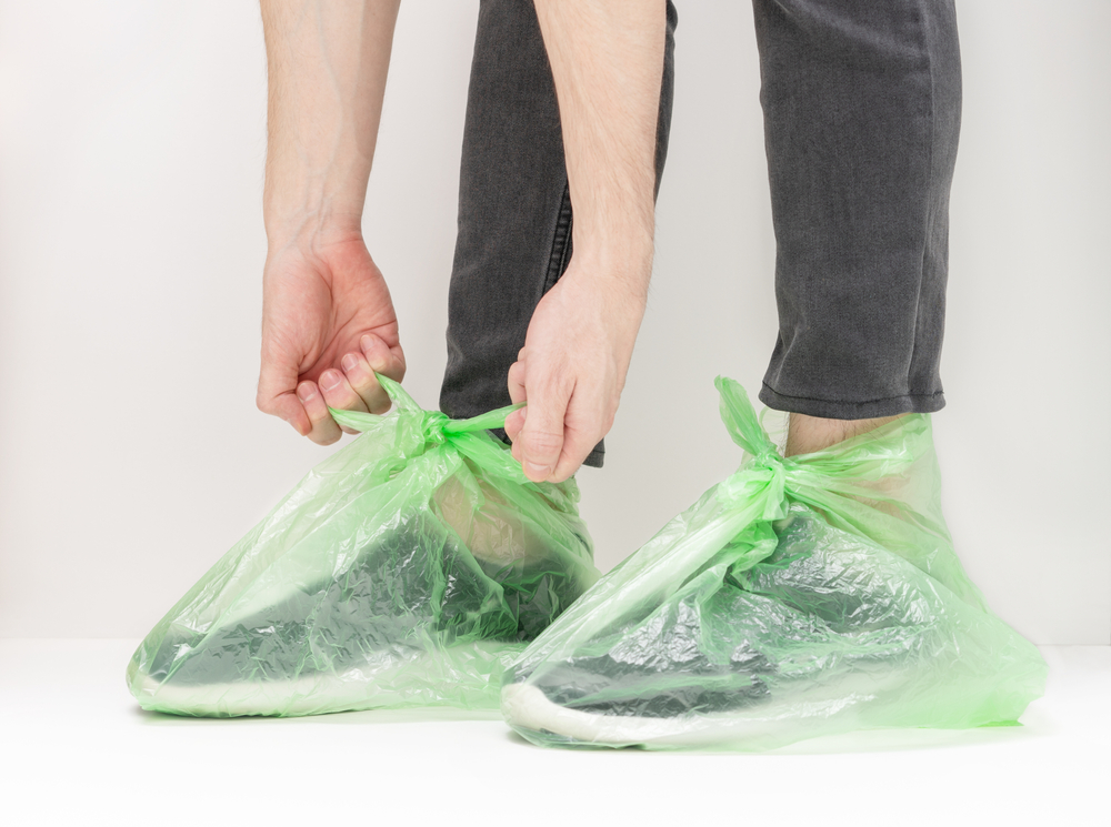 a person tying green plastic bags around their shoes to protect them from dirt or water.