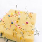 a yellow sponge is used as a makeshift pincushion, holding colorful sewing pins and safety pins.